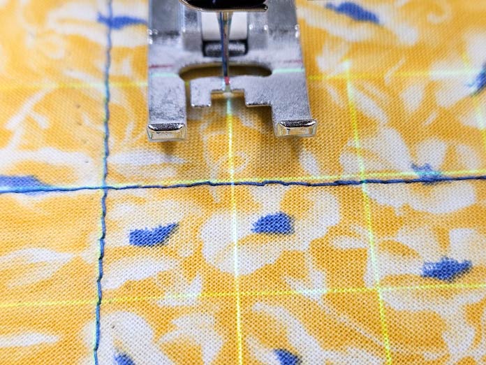 Blue lines of stitching, green projection lines on yellow fabric with a metal presser foot