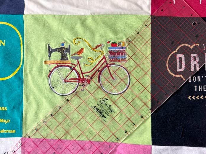 Using a Sew easy Quilting Ruler - 24″ x 61⁄2″ to mark lines on a T-shirt block with a bicycle and sewing machine motif.