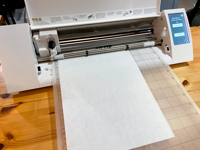 A rectangular piece of freezer paper is shown on the cutting mat of a desktop cutting machine. The machine is sitting on a wooden desk; Sew Easy Freezer Paper for Quilting and Applique