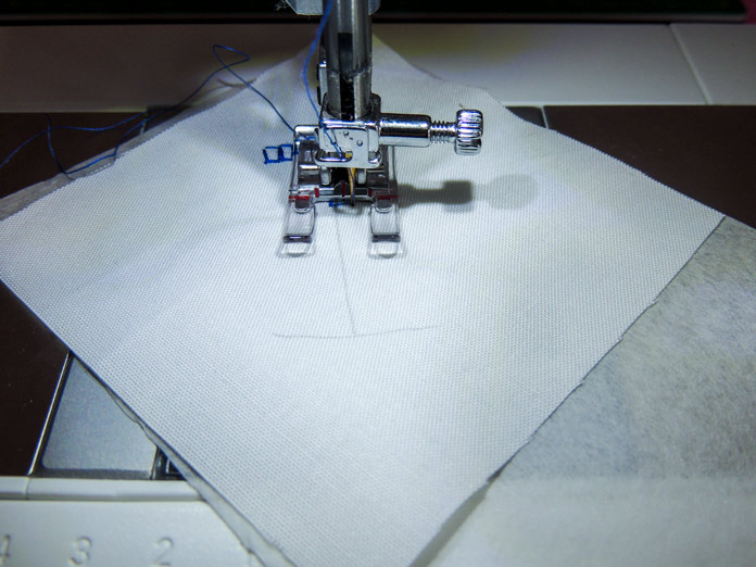 Close-up of stitching area with tear-away stabilizer visible under the fabric square; PFAFF passport 2.0