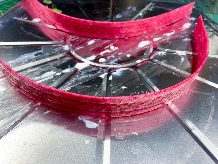 Two pink fabric handles, coated with gel, are shown drying on metal trays with their edges curved. 