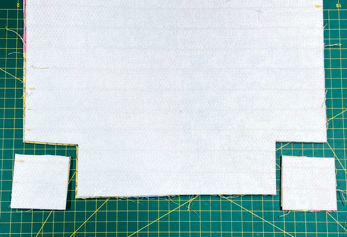 The back side of a quilted panel is shown lying on a green cutting mat. A square has been cut away from the two bottom corners of the panel.
