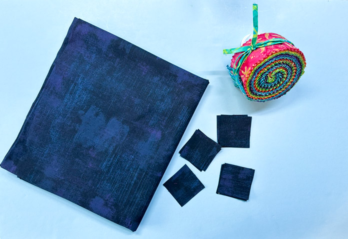 A vibrant rainbow colored jelly roll and mottled navy fabric, with some already cut into 2½" x 2½" squares