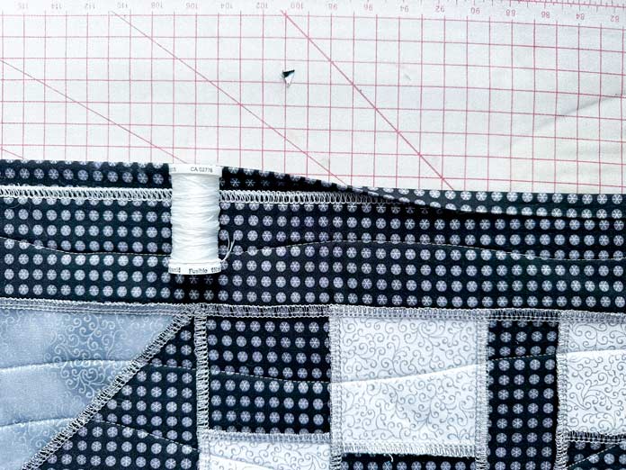 A picture showing the Gütermann spool of fusible thread, next to the black binding half unpressed and half pressed down on the edge of the finished black, gray and white runner.
