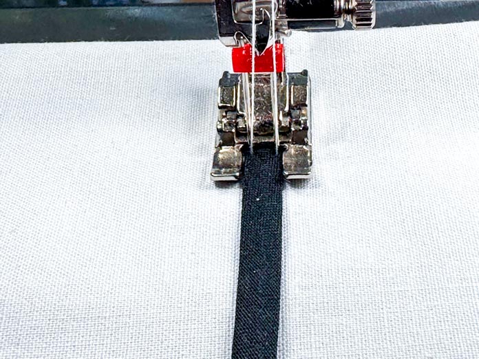 A piece of bias tape is being sewn down using a twin needle.
