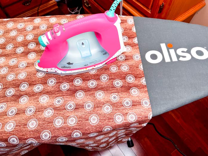 An Oliso Pro Plus Smart Iron pressing a piece of brown/tan fabric.