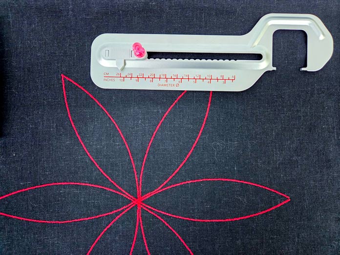 Red stitching on black fabric and a metal sewing machine accessory