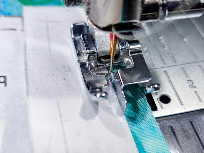A metal presser foot on a sewing machine beside a piece of folded paper