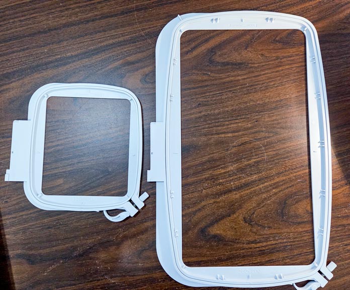 Two plastic machine embroidery hoops on a brown table: HV Designer Topaz 65 