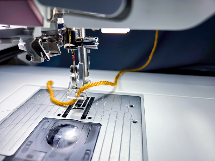 A gold yarn threaded into a plastic foot on a sewing machine