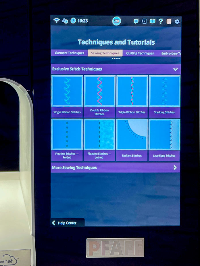 The screen of the PFAFF creative icon 2 sewing and embroidery machine displays the “Techniques and Tutorials” section. The “Sewing Techniques” tab is selected at the top of the screen, highlighted in orange. Below, under the "Exclusive Stitch Techniques" category, nine stitch technique icons are displayed in two rows. Each category is represented by a visual preview showing a stylized stitch on a blue fabric background. At the bottom is a purple bar labeled “More Sewing Techniques.” The navigation area reads “Help Center” in the bottom-left corner. 