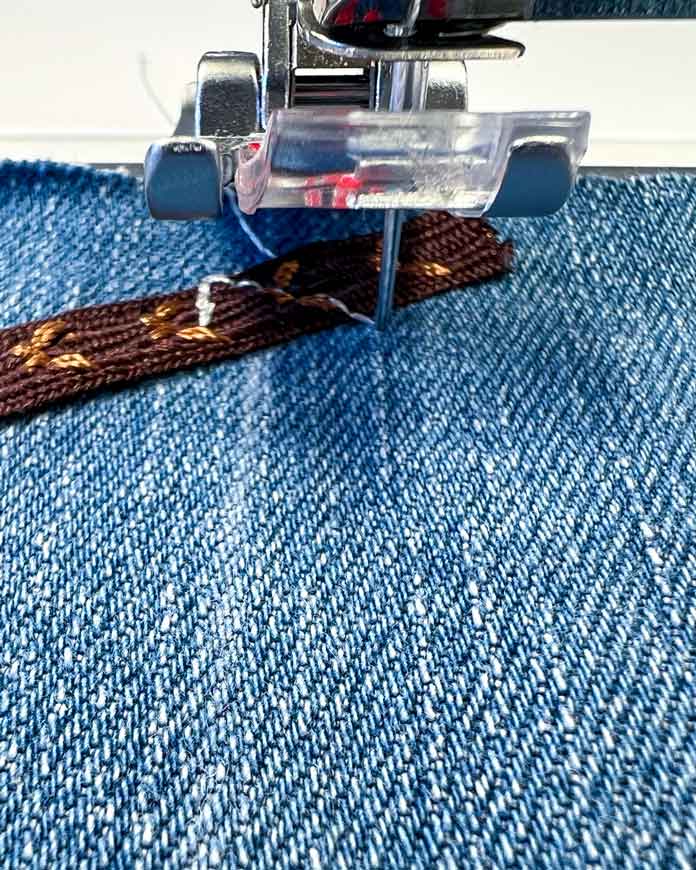 Close-up of the 2A Fancy Stitch Foot on the PFAFF creative icon 2, paused mid-stitch with the decorative lace ribbon lying flat. The stitched line beneath the foot clearly indicates the angle and direction for the next ribbon placement. This is the moment just before placing the second ribbon over the stitching, following the built-in machine prompts.