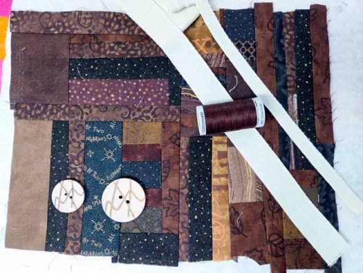 Twill tape, brown thread, and two buttons on scrappy brown fabric