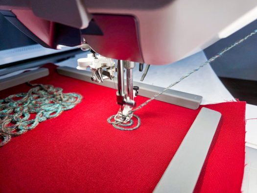 Yarn is being fed into the presser foot on an embroidery machine on red fabric