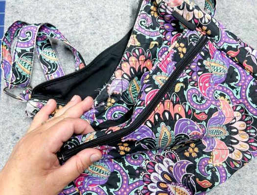 A hand holds the zippered section of a colorful fabric purse.