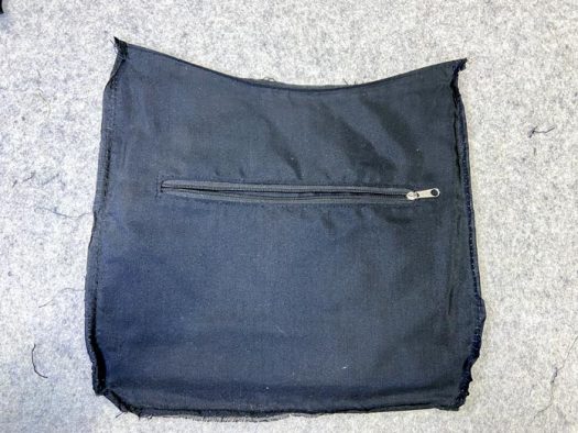 A piece of black lining fabric with a zipper pocket lies on a grey wool pressing mat.