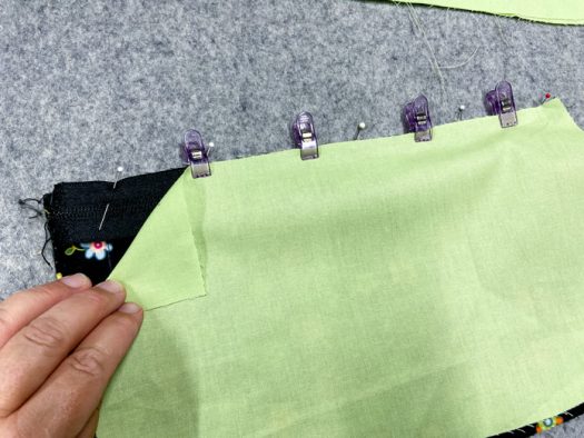 A multicolored quilt block, a rectangle of pink fabric and a stiletto tool all sit on top of a green cutting mat.