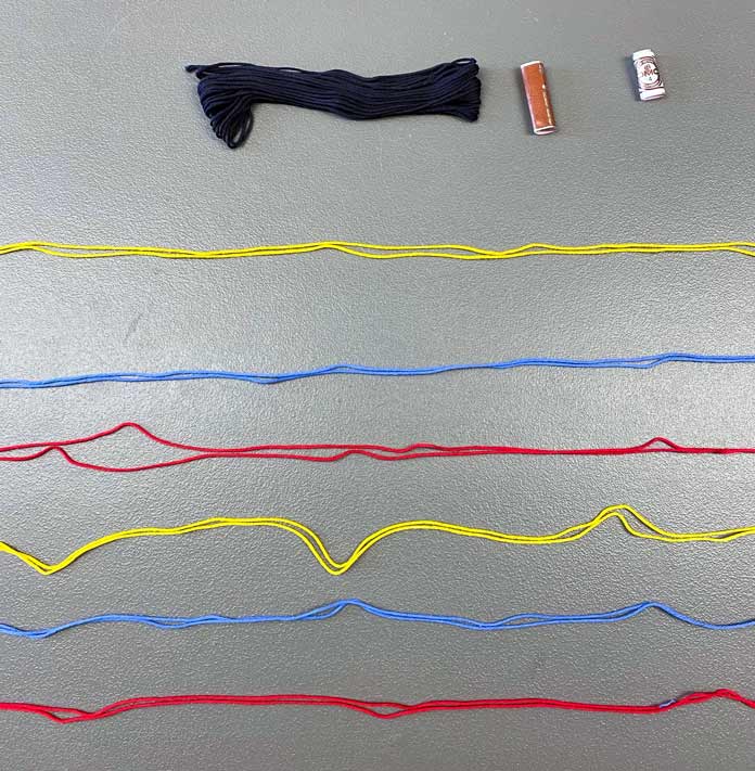 A skein of black floss, and 6 lengths of DMC Matte Cotton Yarn in red, blue and yellow spread across a flat surface; DMC Matte Cotton Yarn