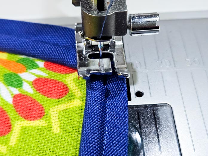 Blue piping on a green fabric under a metal presser foot; Gütermann Nostalgia Box - 50wt Cotton Thread 100m - 48 Shades, Gütermann Nostalgia Box, Flat Felled Foot 9mm, Husqvarna VIKING Opal 690Q, free sewing pattern, outdoor accessories, outdoor cushions, piping, Husqvarna VIKING 8” Bent Trimmer