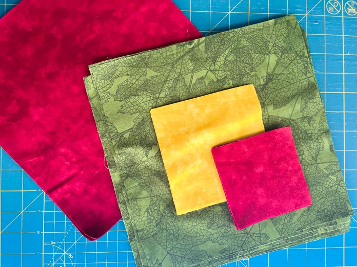 Red, yellow and green fabrics are cut and ready for quilt construction. OLFA Rotary Circle Cutter, OLFA 45mm Splash™ Handle Rotary Cutter, OLFA 45mm Tungsten Tool Steel Rotary Blade, OLFA 12½” Square Frosted Acrylic Ruler, OLFA 6” x 12” Frosted Acrylic Ruler, OLFA 6” x 24” Frosted Acrylic Ruler, OLFA 24” x 36” Double Sided rotary Mat, Heatnbond Non-woven Lightweight Fusible Interfacing, Oliso PRO™ TG1600 Pro Plus Smart Iron