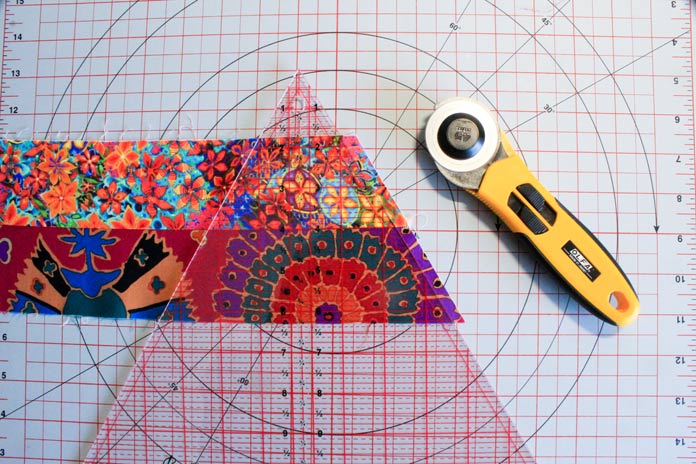 Ready to trim off the excess fabric on the edge of two strips sewn together using a triangle ruler, rotary cutter, and cutting mat; Komfort Kut 360° Rotating Cutting Mat - 18" x 18", Sew Easy Triangle Ruler 60°, OLFA Quick Change Rotary Cutter