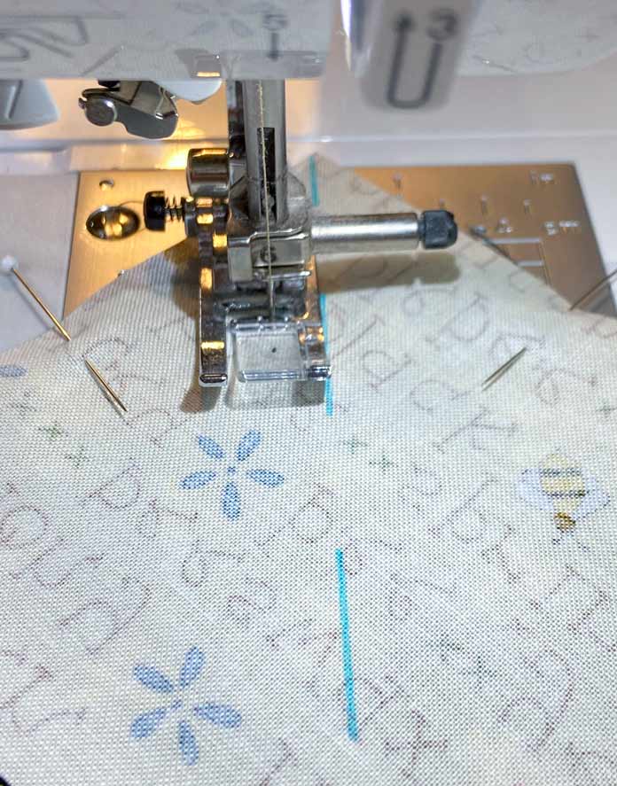 A close-up of the J foot on the Brother NQ900 sewing machine. One side of the foot is lined up with the blue diagonal line on the back of the yellow fabric.