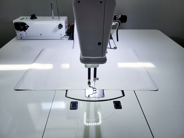 A sheet of silicone lies behind the needle and the Stitch Regulation sensors on a white stationary sewing table with sewing machine; Husqvarna Viking PLATINUM™ Q160