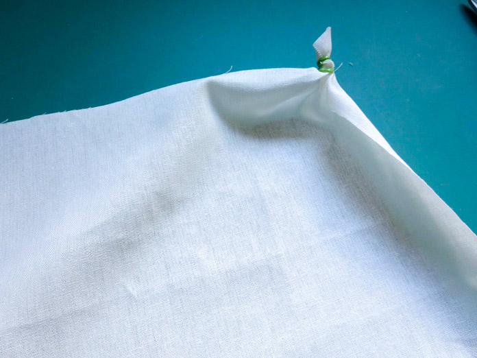 White fabric is pinched in one corner and secured with elastic