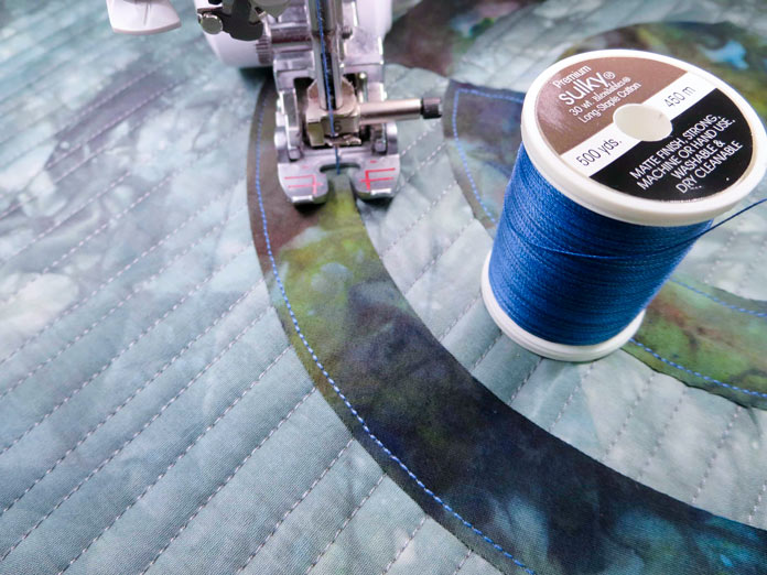 A walking foot is used to stitch the arcs to the background fabric using blue Sulky Blendables 30wt thread.