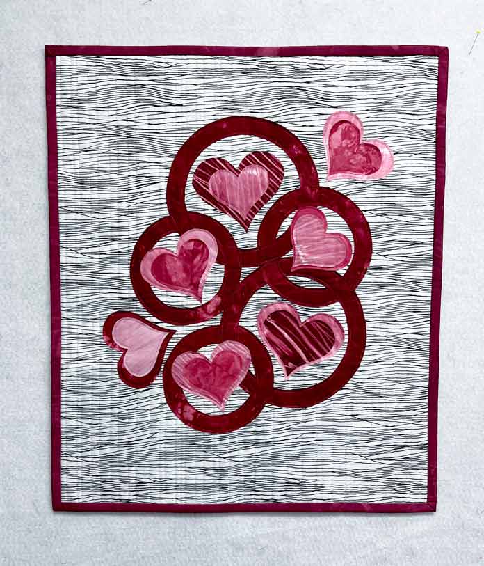 Finished quilt with 7 appliqued hearts and 5 appliqued circles in red and pink fabrics