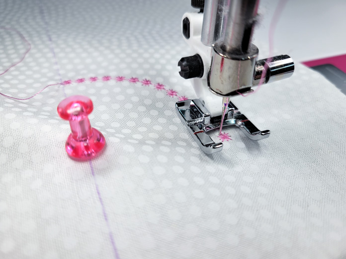 A pink push pin and a sewing machine presser foot on white fabric; Husqvarna Viking Designer EPIC 2