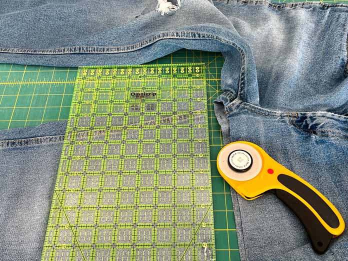 An OLFA 8½” x 24 ruler and an OLFA 60mm rotary cutter on a pant leg of a pair of jeans. 