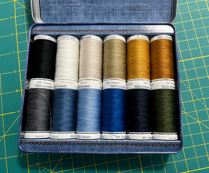 The Gütermann Denim Love Nostalgia Box with 12 colorful spools of thread is open on a green cutting mat.