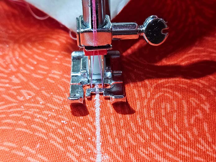 A white line of stitching, a twin needle, a metal presser foot on orange fabric; making a project bag using Güterman Thread and the Husqvarna VIKING ONYX 25