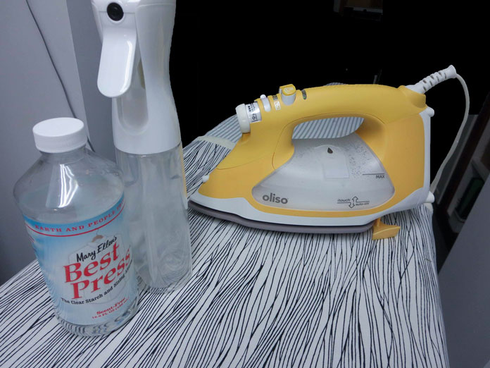 OLISO PRO Iron in yellow, a bottle of Mary Ellen’s Best Press and a Spray and Misting Bottle; OMNIGRIP Ruler 8½" x 8½", OLFA 45 mm Ergonomic Rotary Cutter, OLFA Endurance Rotary Blades, Sulky Tear-Easy Stabilizer, Odif 505 Adhesive Fabric Spray, OLISO PRO TG1600 Pro Plus Smart Iron, Mary Ellen’s Best Press, Best Press Spray and Misting Bottle