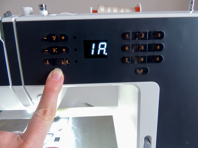 Finger pressing the information (i) button and display showing the presser foot number and the IDT dot