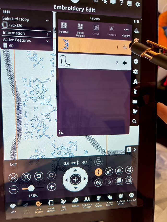 A stylus touching the PFAFF creative icon 2 sewing machine 10.1-inch capacitive touch screen to choose the layers of an embroidery; PFAFF creative icon 2, PFAFF Universal Needles Size 80/12, PFAFF Universal Needles Size 90/14, PFAFF Quilting Needles Size 90/14, PFAFF 6D Dynamic Spring Foot, PFAFF creative 120 Square Hoop (120 x 120 mm), Mettler 40wt polyester thread, PFAFF Aqua Magic Plus Stabilizer, PFAFF 0A Standard Presser Foot for IDT System