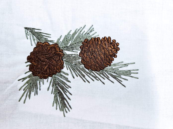 Brown pine cones and pine needles on white fabric; Fairfield Poly-Fil, Fairfield Low-Loft, Fairfield Traditional, Fairfield Quilter’s 80/20 Quilt, Fairfield Toasty Cotton Natural, and Bosal Katahdin Batting Strip, SEW EASY Freezer Paper for Quilting, UNIQUE Easy Stitch Perforated Embroidery Backing, UNIQUE Rinse Away Water Soluble, UNIQUE SEWING Tear Away Embroidery Backing, UNIQUE Trace Away Water Stabilizer Film, HEATNBOND Stitch n Sew Tear-Away Stabilizer, Sulky Cut-Away Soft ‘n Sheer, Sulky Cut-AwayPlus, Sulky Super Solvy, Sulky Super Solvy, Sulky Ultra Solvy, Sulky Fabri-Solvy, Sulky Ultra Solvy, Sulky Stick ‘n Carve, Sulky Stick ‘n Stitch, SULKY Sticky + Tear-Away, Sulky Totally Stable, Sulky FUSE ‘n STITCH, Sulky Tender Touch, Sulky Tear-Easy, Sulky Stitch ‘n Seal, Sulky Heat-Away