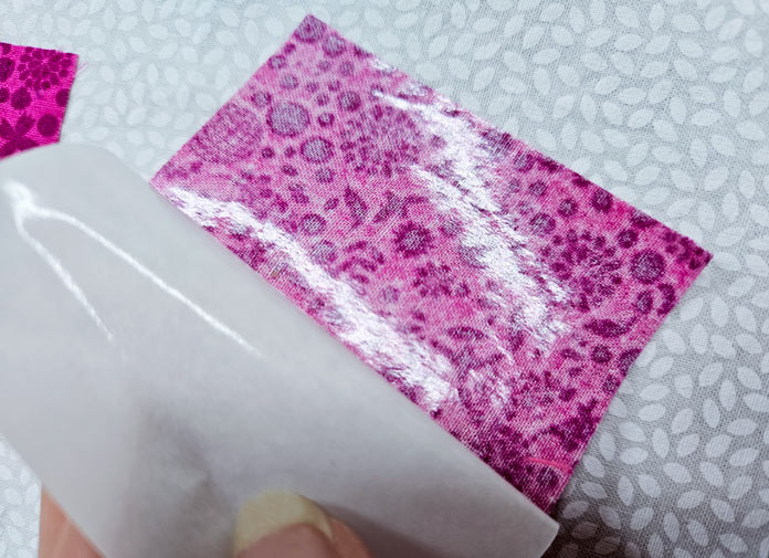 A pink square of fabric on white fabric; Learn how to use HeatnBond SOFTSTRETCH fusible web on knits, denim, fleece, and more