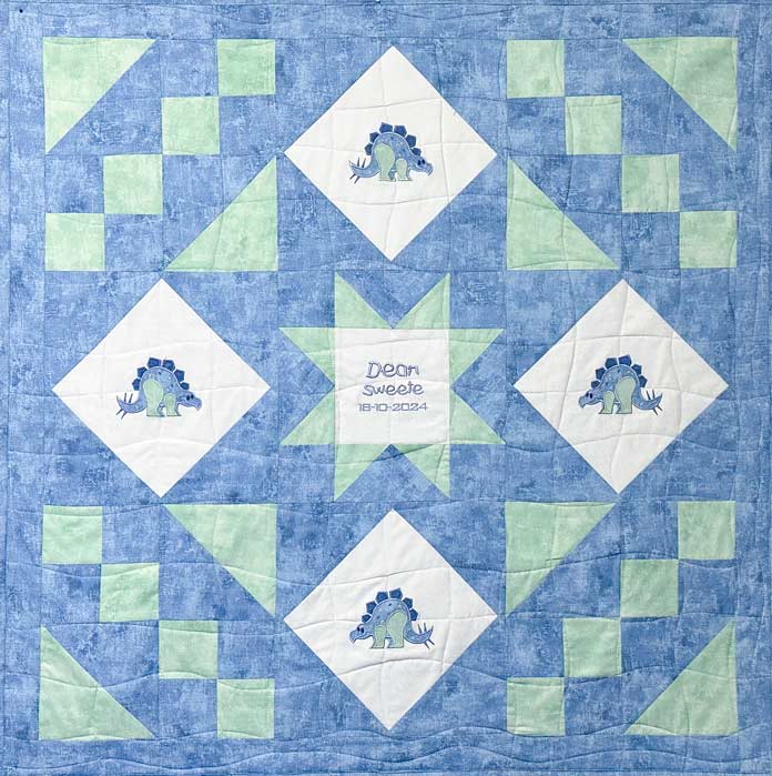 A blue and green pieced quilt with white diamond with a blue and green appliqued dinosaur, quilted in wavy lines finished and bound with a blue quilt binding; PFAFF creative expect 350, sewing machine reviews, mySewnet Quilting Software, mini quilt finishing, beginner quilting tips, quilt binding guide, machine quilting techniques, organic quilting, embroidery quilt labels, diy quilt projects, free motion quilting, free quilting project, free quilting patterns, baby quilt, free quilting tutorials