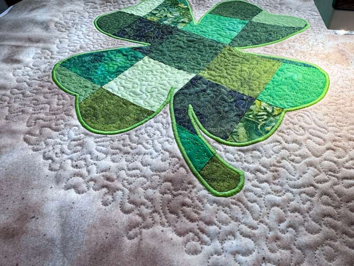 The stipple stitch applied to the four-leaf clover design is featured in a partially quilted clover quilt. 