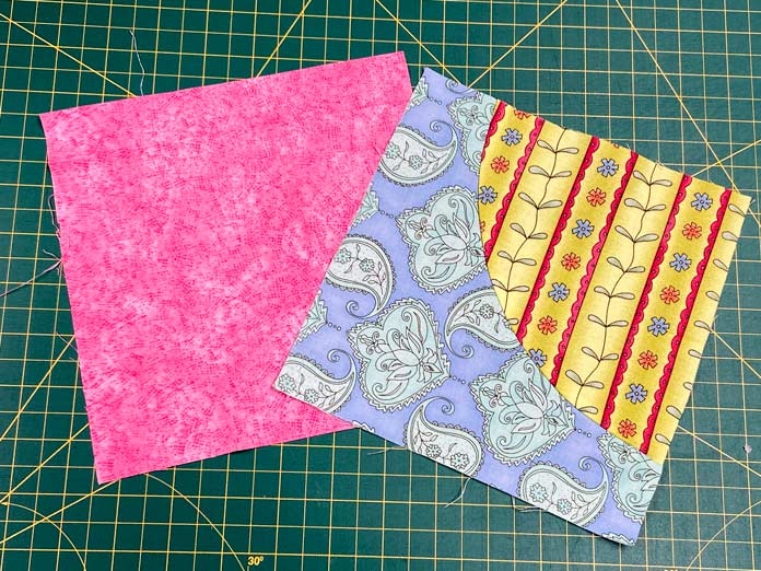 A square of pink fabric and a multicolored quilt block sit on top of a green cutting mat.