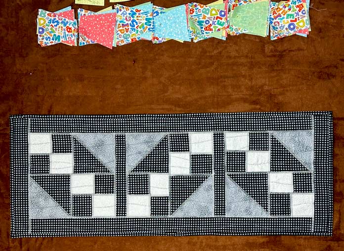 Black, gray and white runner with exposed decorative seams shown finished with binding fused in place.