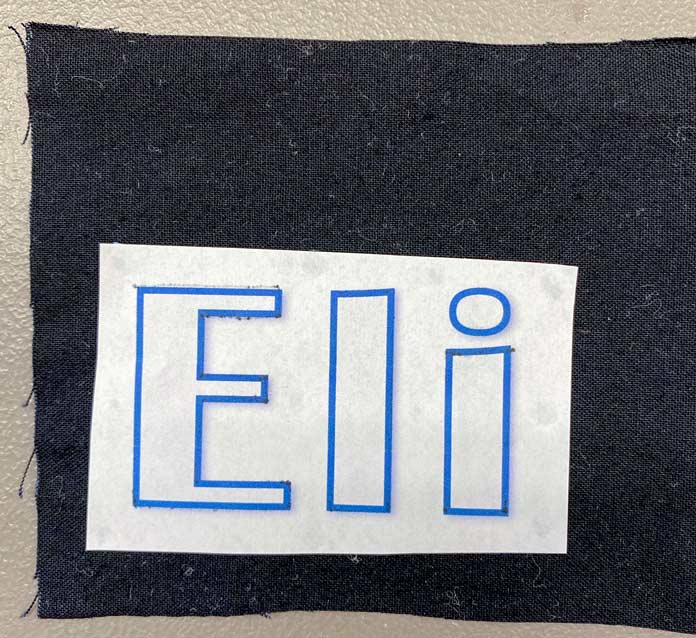 The name Eli printed on white paper laid out on black fabric