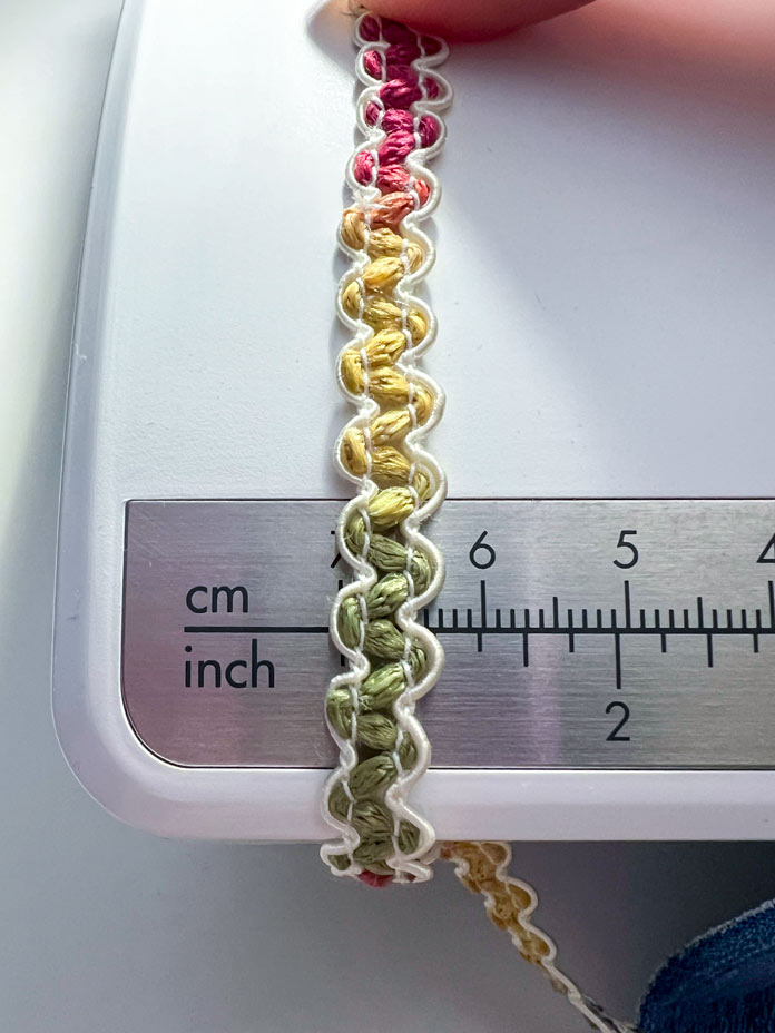 The multicolored lace, approximately 5 mm wide, is shown aligned for measurement on the PFAFF creative icon 2 accessory tray.