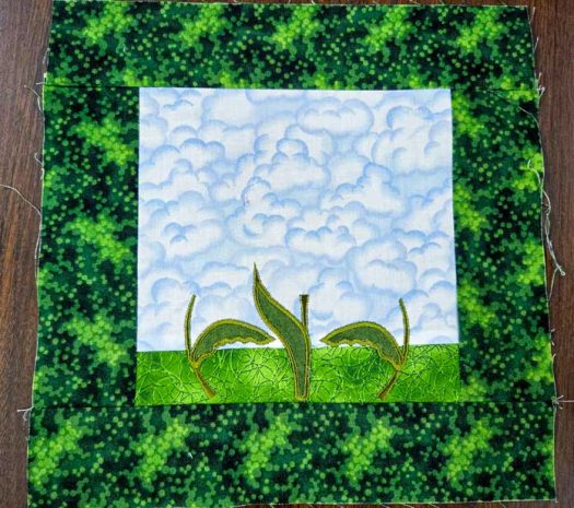 A green and blue fabric with three green stems and leaves