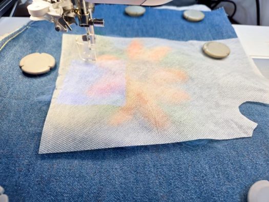 A piece of white fabric on denim in a metal machine embroidery hoop