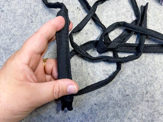 A hand holds a section of black binding tape. More of the tape lays on a grey wool pressing mat.