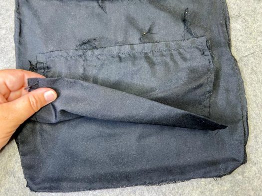 A hand holds the free-hanging lining of the zippered pocket that is inset into the lining of the purse.