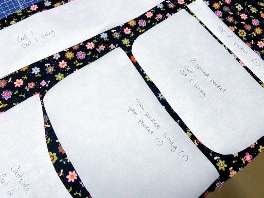 Multiple labelled pattern pieces made of freezer paper lie on top of black floral fabric.